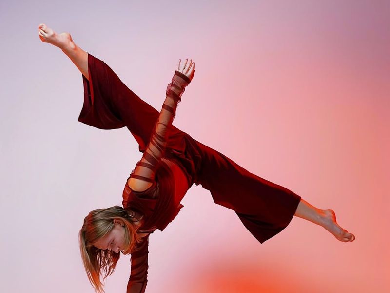 Woman performing a flowing yoga movement in a spacious, light-filled studio.